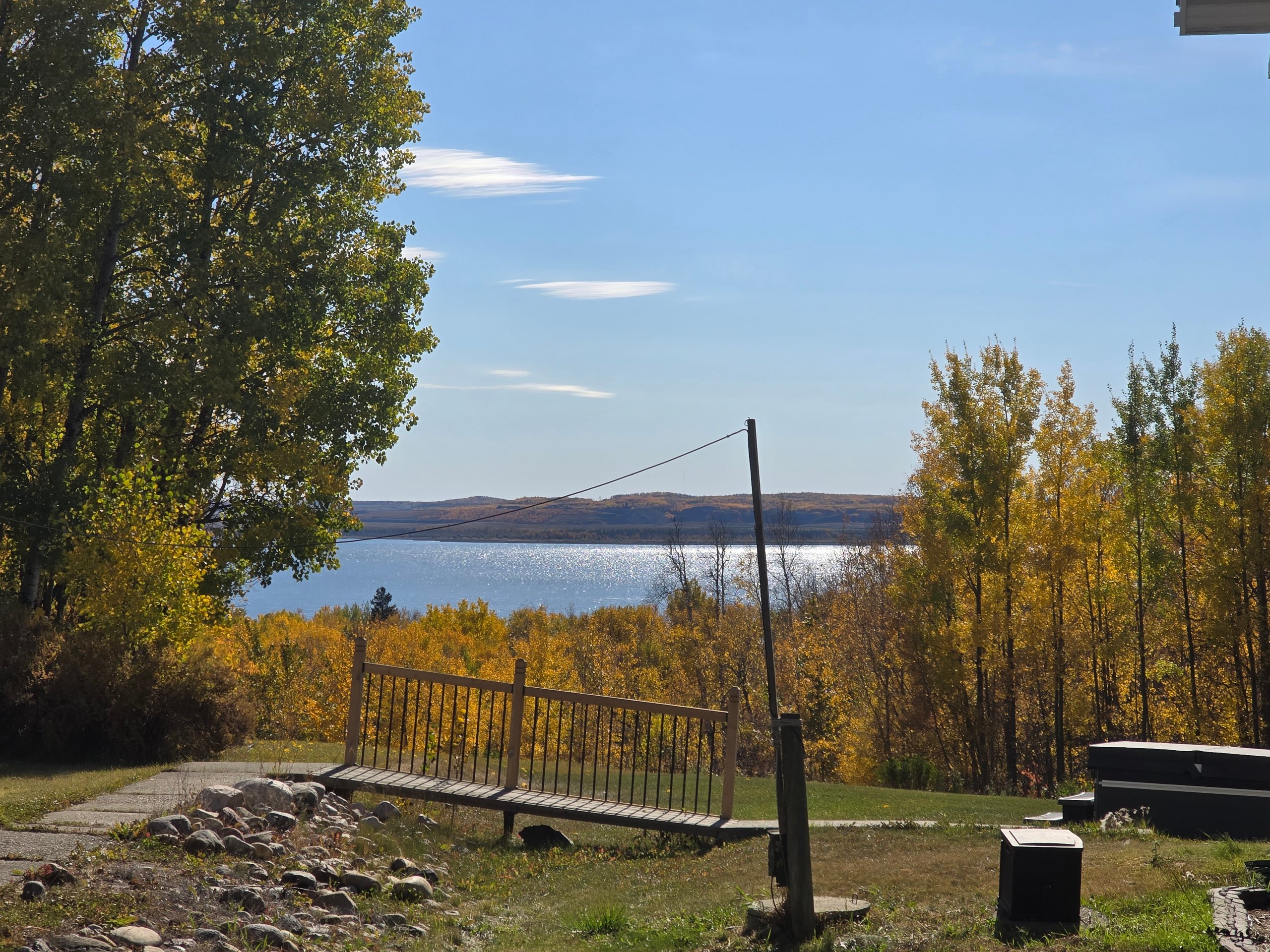 Autumn trees with yellow leaves overlooking a sparkling lake under a clear blue sky.