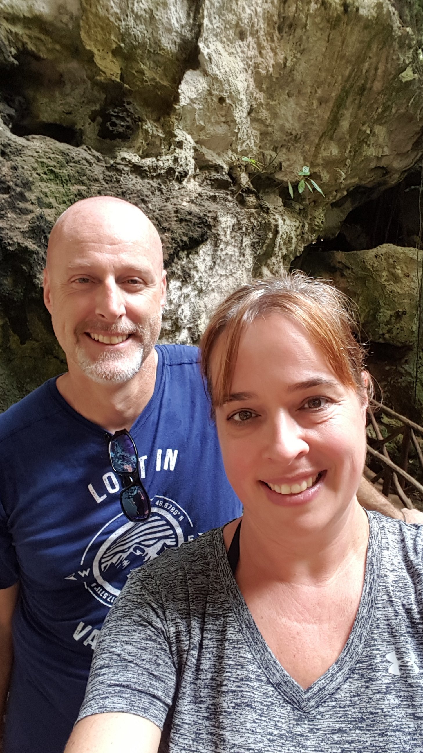 Smiling man and woman taking a selfie in a rocky cave setting.